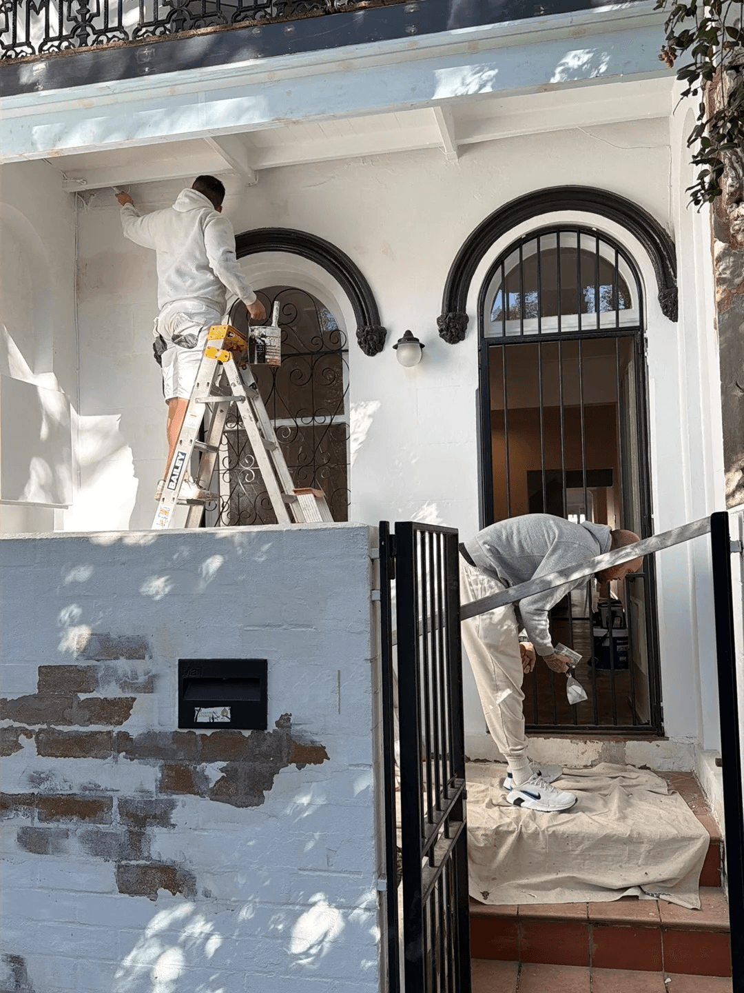 Two painters working on the verandah and entry of a Victorian terrace, with the tiled front steps covered